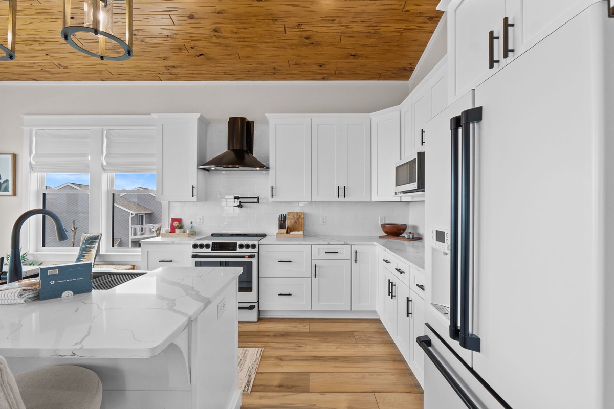 Imagine preparing your favorite meals in this bright, modern kitchen with sleek white cabinetry, stainless steel appliances, and stunning wood-planked ceilings that add warmth to your culinary adventures.