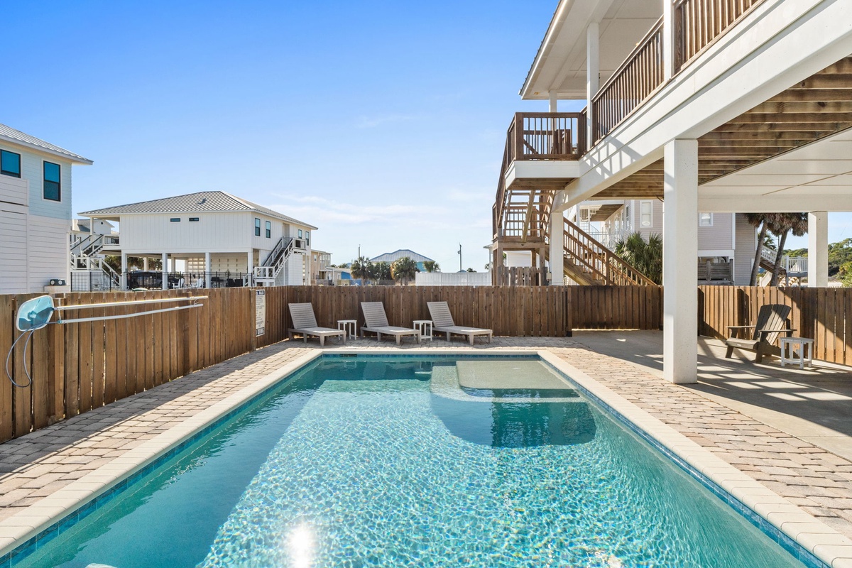Your private pool awaits with sparkling waters, sunny lounging areas, and a peaceful fenced yard beneath clear blue skies.