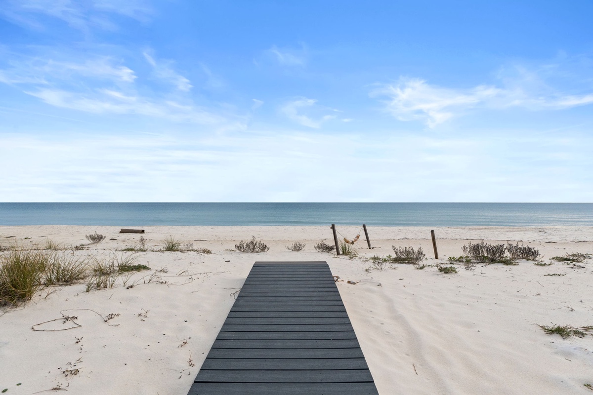 Pristine beachfront with wooden walkway leading to crystal-clear waters under endless blue skies.