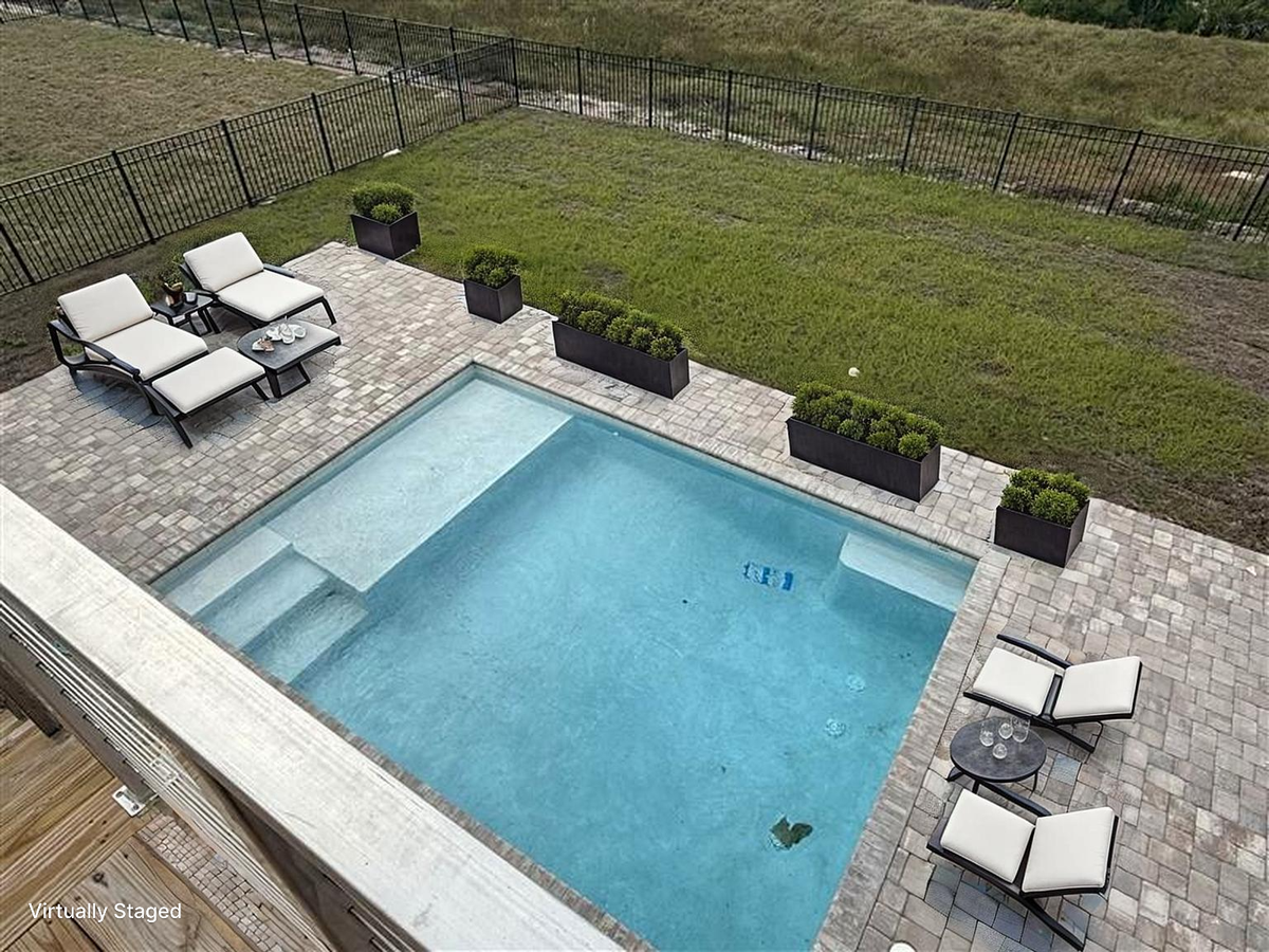 Aerial view of the private pool area with lounge seating, decorative planters, and spacious paved deck surrounded by fenced yard.