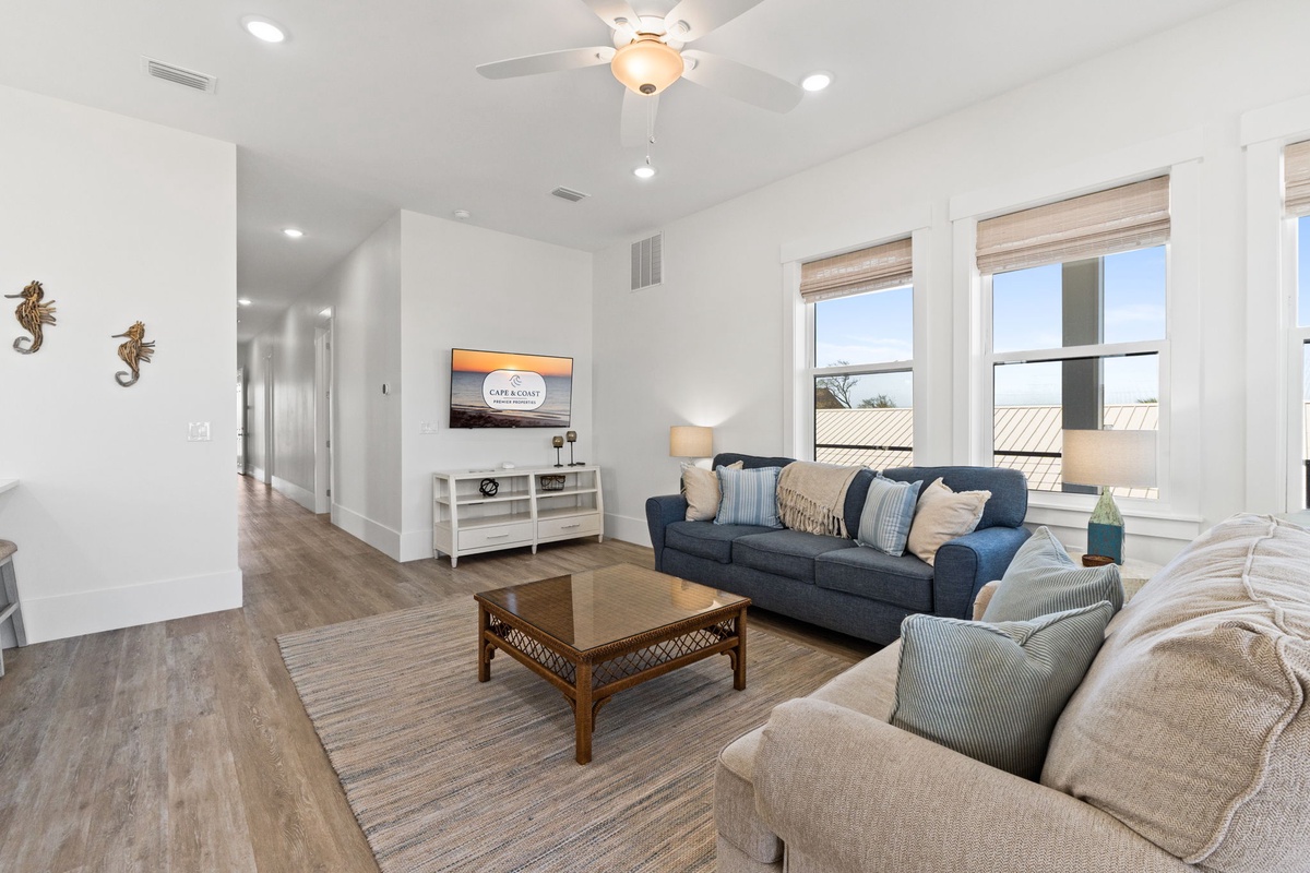 Sink into plush coastal seating where natural light floods your comfortable gathering space through oversized windows.