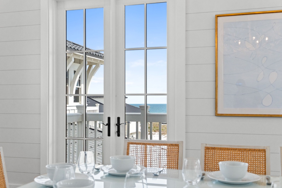Picture yourself enjoying morning coffee at this elegant dining table, with the bright blue sea framing your view through tall French doors. Coastal elegance meets comfortable living.