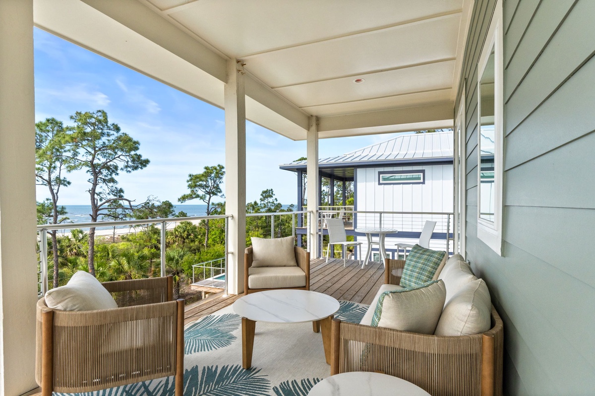 Unwind in your private covered terrace with ocean glimpses through coastal trees, featuring comfortable seating perfect for morning coffee or evening relaxation.