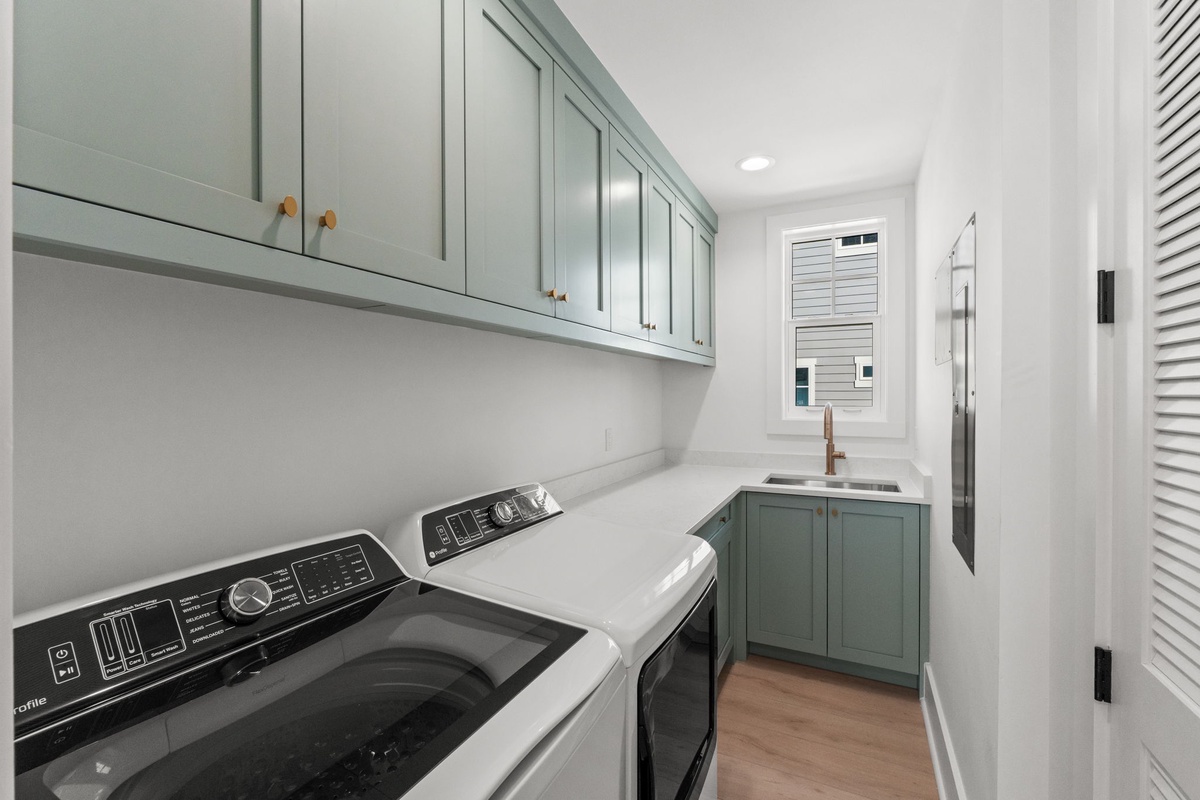 Your thoughtfully designed laundry room features custom sage-green cabinetry, marble countertops, and a convenient utility sink for all your washing needs.