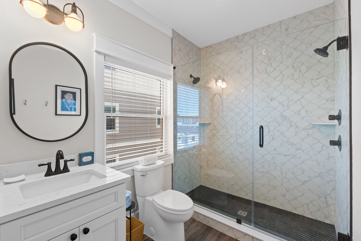 Your spacious bathroom features a walk-in shower with elegant marble-look tile, modern fixtures, and natural light streaming through the windows—perfect for refreshing mornings.