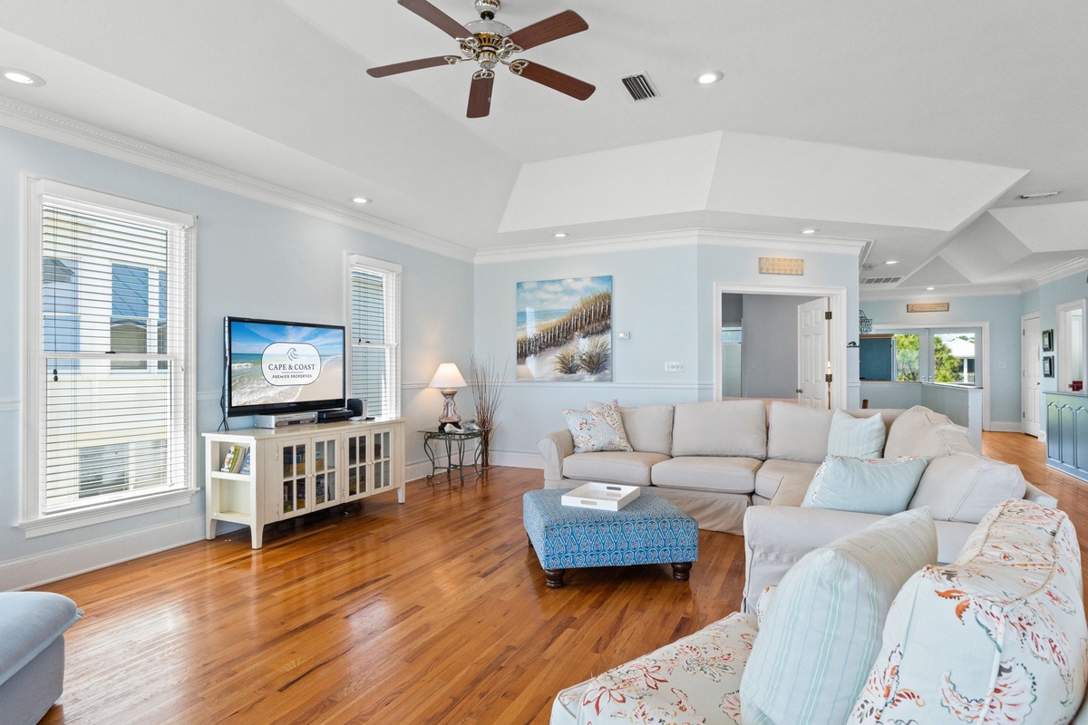 Unwind in your spacious living room featuring coastal-chic décor, plush sectional seating, and warm hardwood floors beneath soaring ceilings.