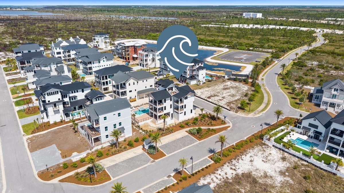 Aerial view of a modern coastal neighborhood with multi-story beach houses featuring pools and tropical landscaping.