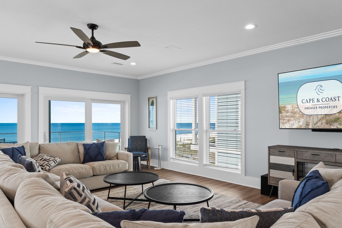 Relax in this bright, coastal living room where floor-to-ceiling windows frame stunning ocean views. Plush seating, soothing colors, and gentle breezes from the ceiling fan create your perfect beach getaway.