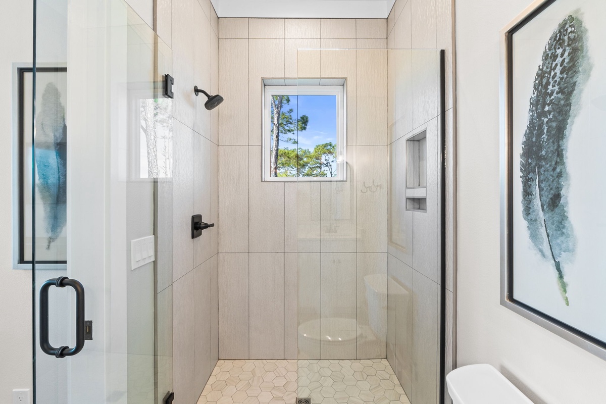 Step into your spa-like shower with elegant tiling and a peaceful window view of lush greenery.
