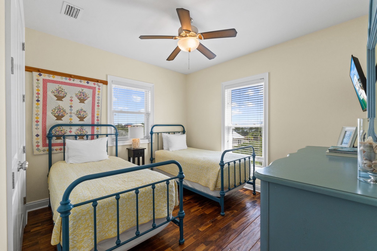 Your charming guest room features twin beds with vintage-inspired frames, warm hardwood floors, and coastal decor that creates a cozy, relaxing atmosphere for restful nights.