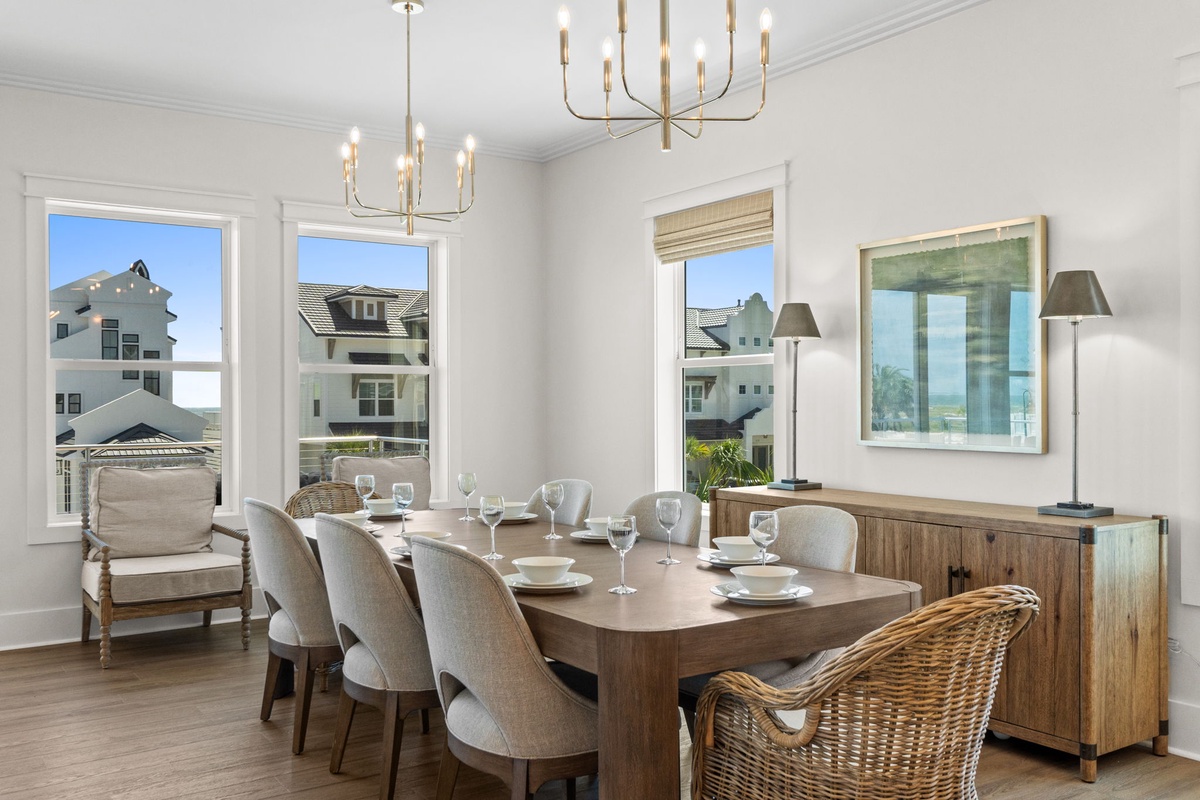 Gather around this elegant dining table for memorable meals with your group, bathed in natural light from expansive windows and the warm glow of modern chandeliers overhead.
