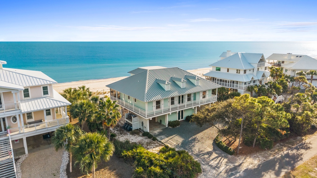 Aerial view of beachfront vacation homes nestled among palm trees, just steps from pristine sandy shores and turquoise waters.