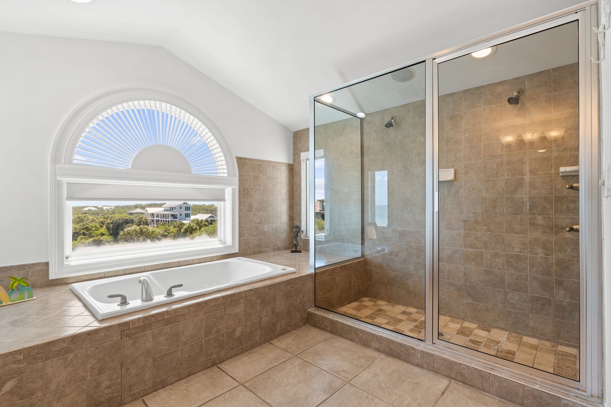 Picture yourself soaking in this tiled tub while gazing through the arched window at coastal views, then stepping into your spacious walk-in shower to refresh—a truly serene retreat.