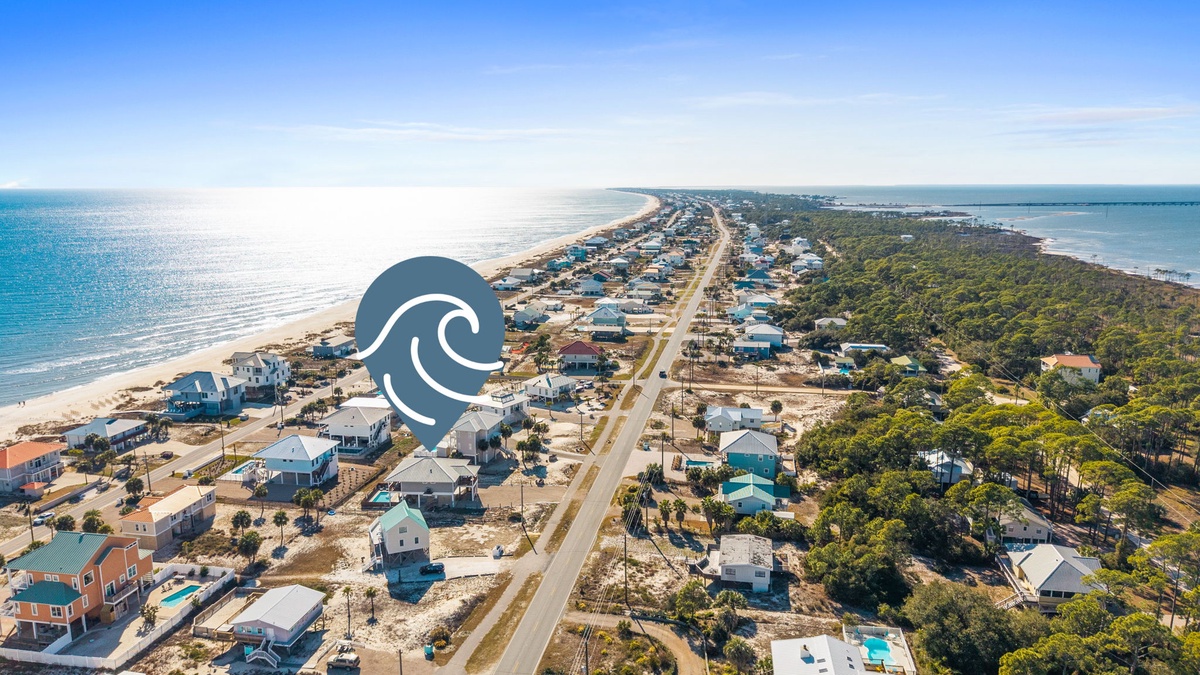 Aerial view of a coastal community with beachfront homes, tree-lined neighborhoods, and pristine sandy shores stretching along crystal-clear waters.