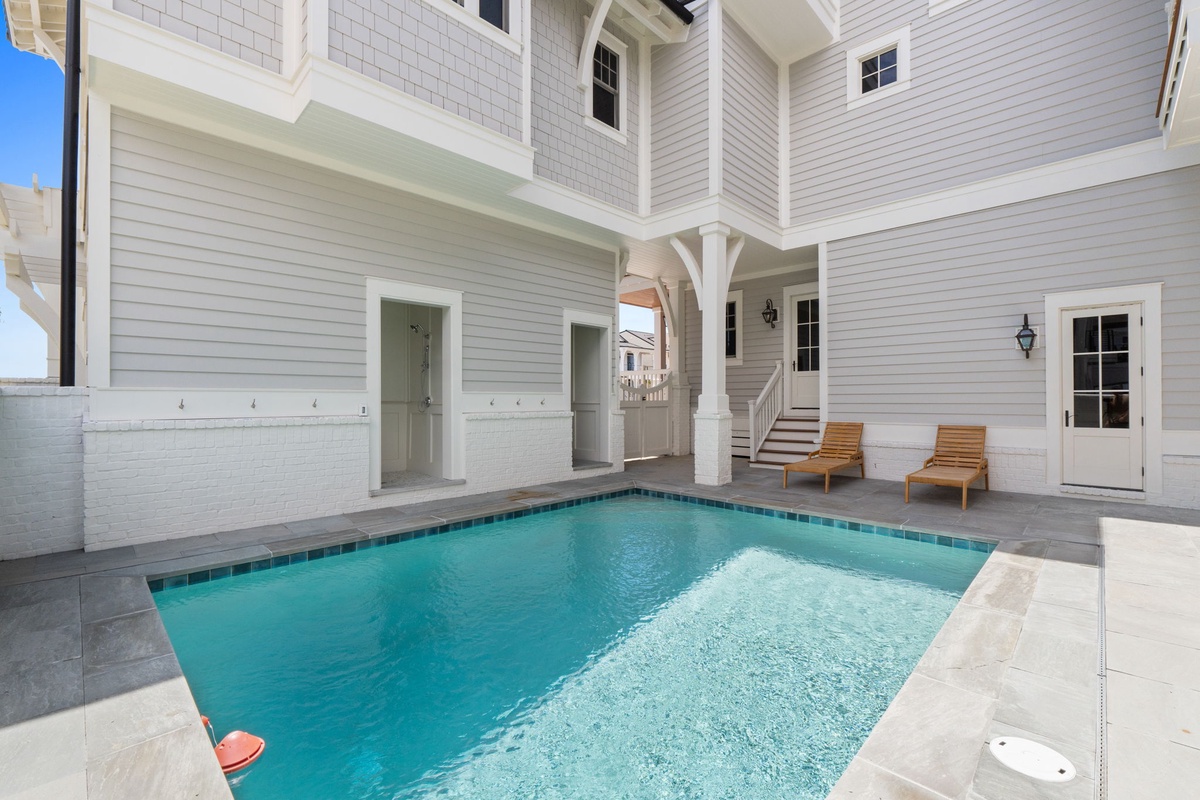This private courtyard pool offers a serene retreat surrounded by elegant coastal architecture, with sunny lounge chairs and a charming archway framing the space.