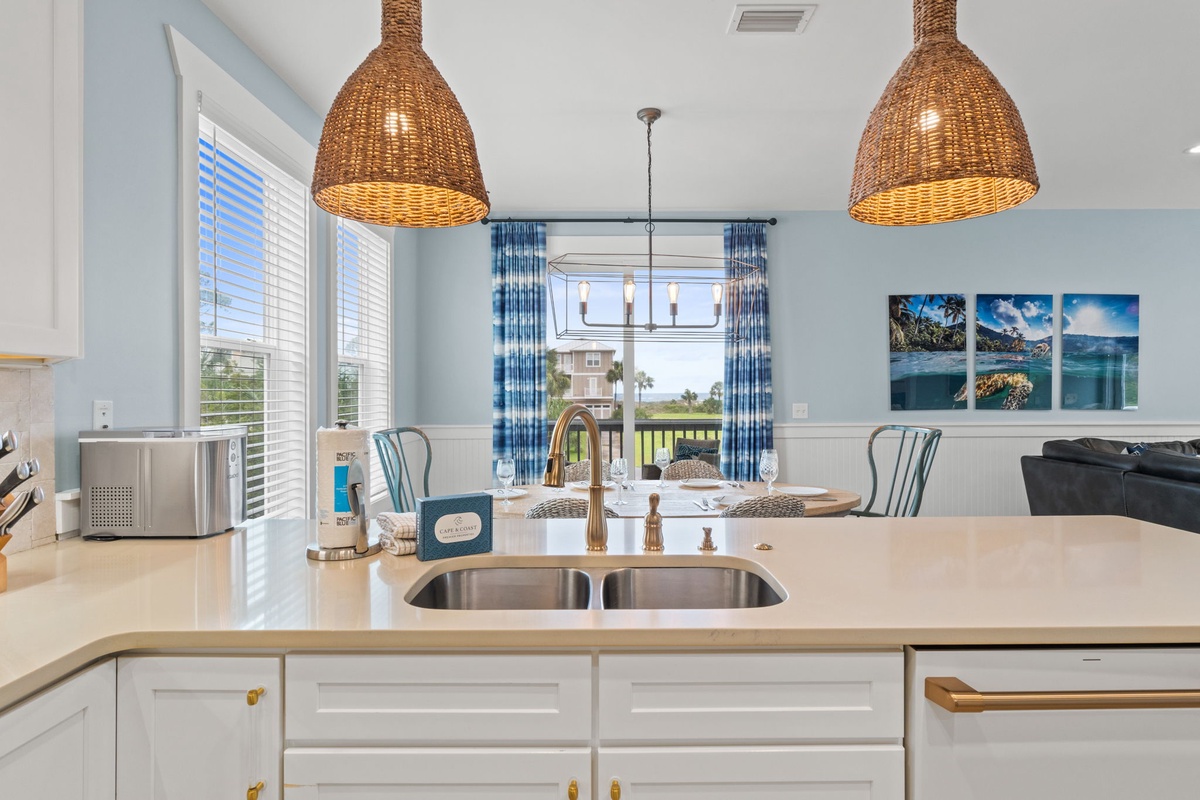 Picture yourself prepping meals in this bright coastal kitchen, where gleaming countertops and woven pendant lights frame gorgeous views of lush green landscape through the dining area windows.