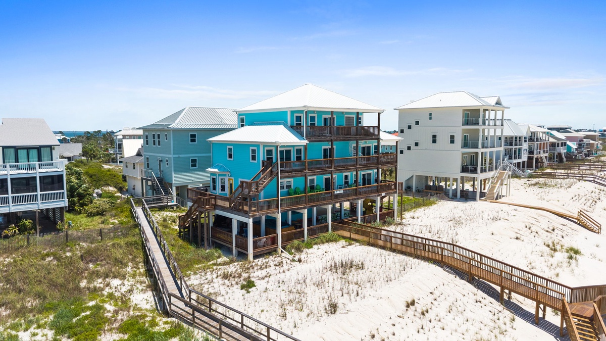 Aerial view captures a vibrant turquoise beachfront property with multiple balconies, nestled among coastal homes on pristine white sand—steps from the shore.