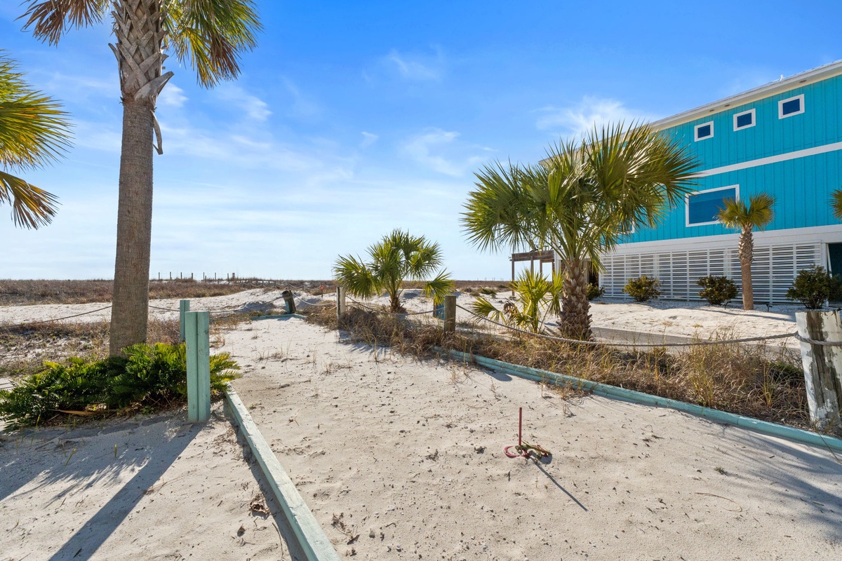 Bright turquoise beach house surrounded by swaying palms and sandy paths leading to coastal adventures.