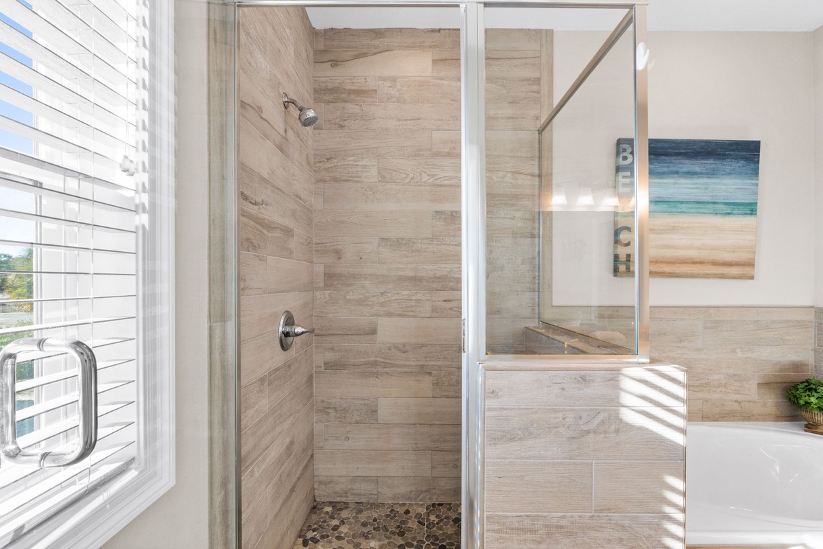Refresh in your spa-like shower with wood-look tiles and pebble floor, surrounded by natural light streaming through shuttered windows.
