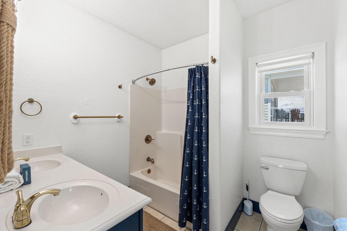 Your bright, nautical-themed bathroom features a full tub-shower combo, gold fixtures, and a charming anchor-patterned curtain to complement your coastal getaway.