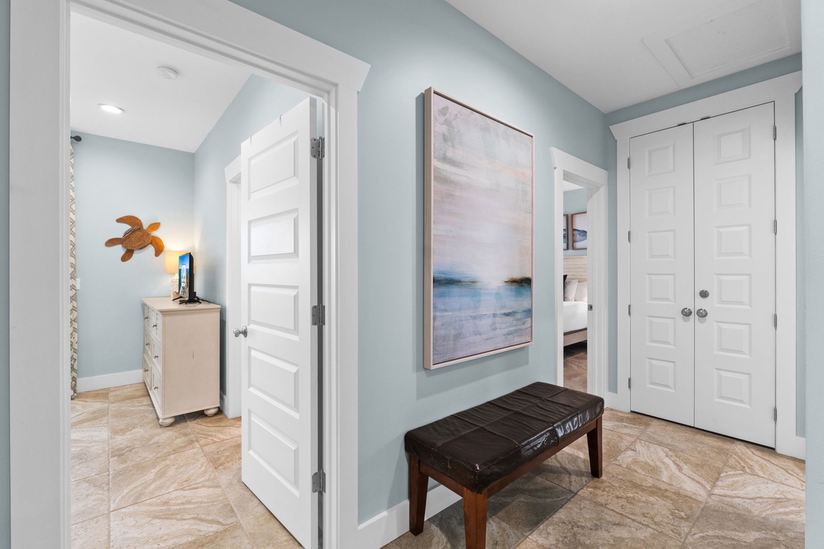 Step into this calming coastal hallway where soft blue walls and beach-inspired art welcome you home. A cozy bench invites you to pause while seaside decor hints at the peaceful retreat awaiting inside.