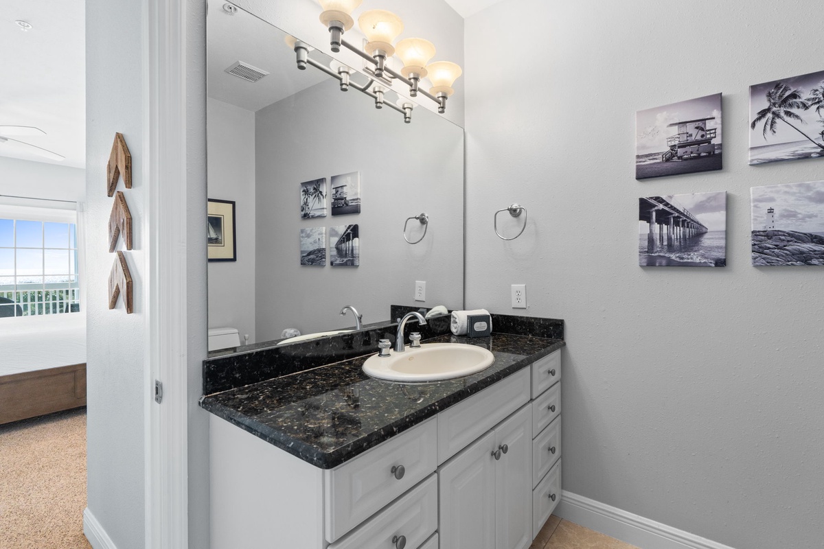 Freshen up at your stylish vanity with luxurious granite countertops and elegant coastal artwork creating a serene atmosphere.