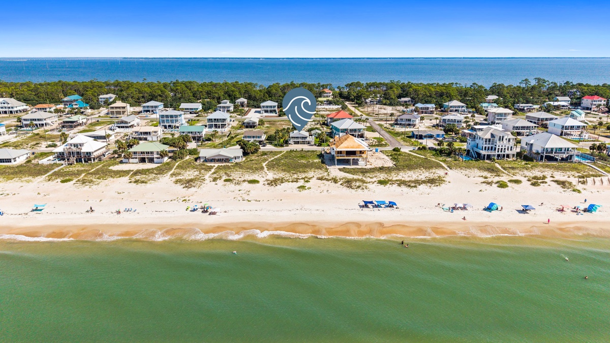 Aerial view of a beachfront community nestled between calm ocean waters and coastal landscape, offering easy access to sandy shores and seaside relaxation.