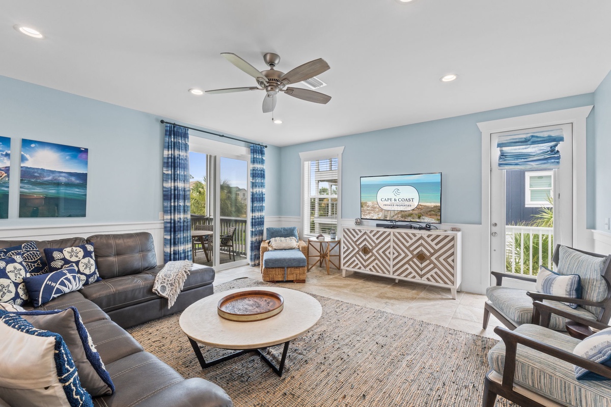 Unwind in your bright coastal living room with plush seating, ceiling fan, flat-screen TV, and doors opening to your private balcony overlooking the scenery.