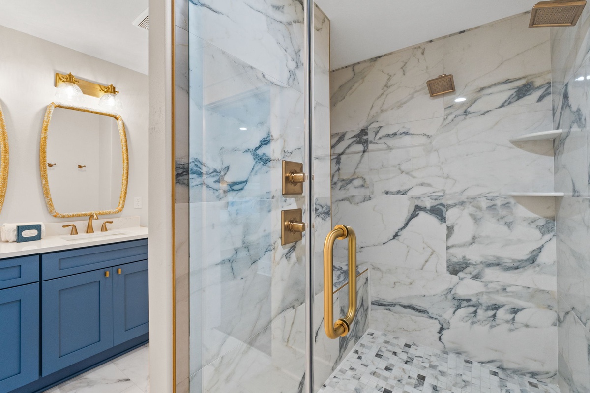 Elegant marble bathroom with gold fixtures creates a luxurious retreat. Your private shower features dual rainfall heads, built-in shelving, and a designer mosaic floor.