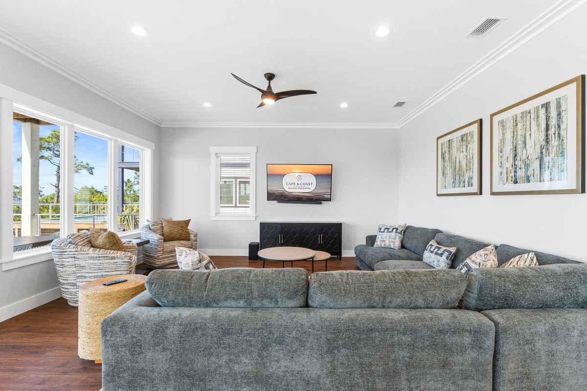 Sink into plush sofas in your bright living room where coastal artwork and a ceiling fan create perfect comfort for relaxing evenings.