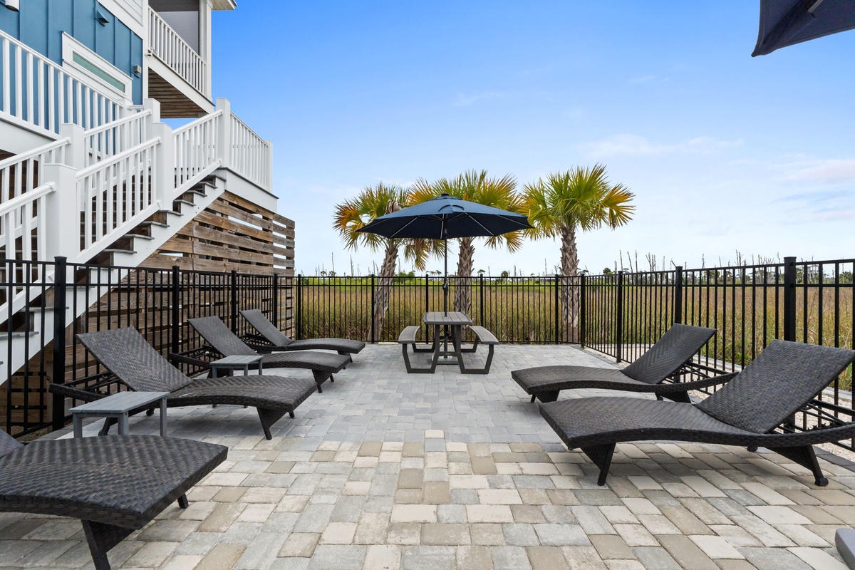 Spacious patio with multiple lounge chairs, picnic table, and umbrella creates the perfect outdoor relaxation space under sunny skies.