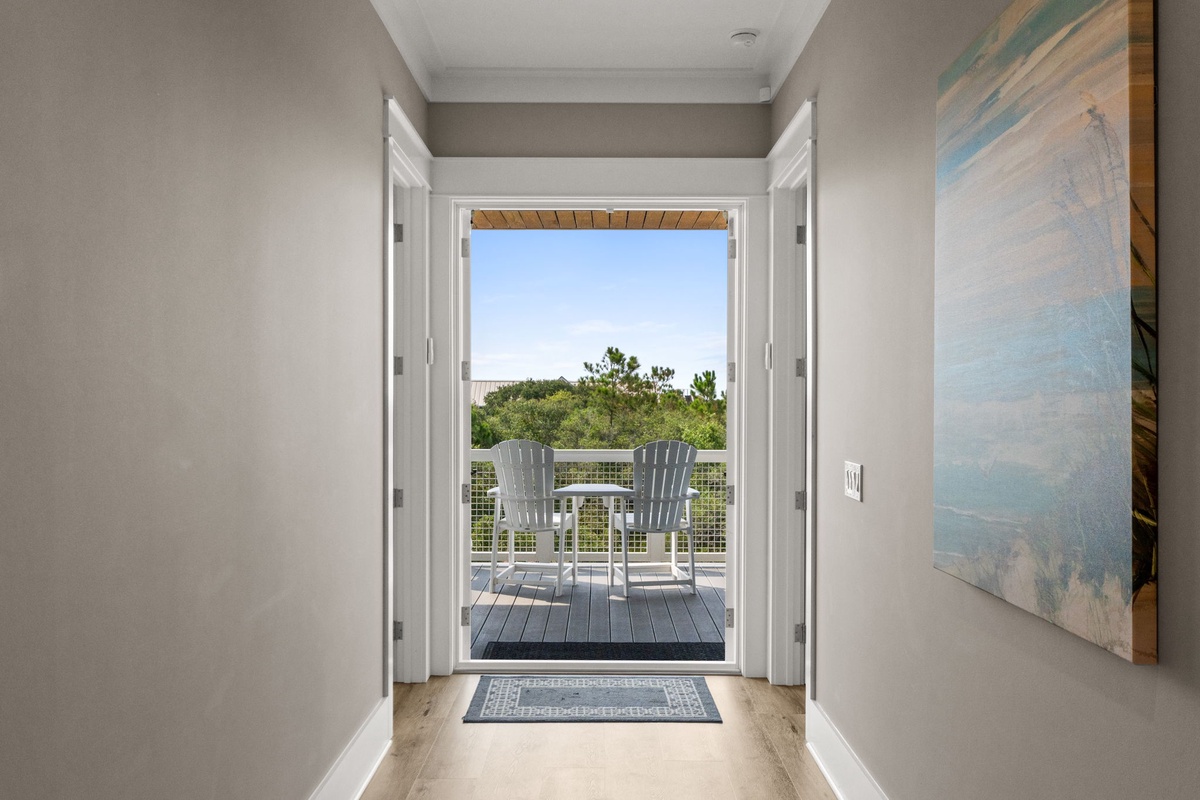Step through these doors onto your private balcony, where white Adirondack chairs await and lush greenery frames peaceful blue skies.