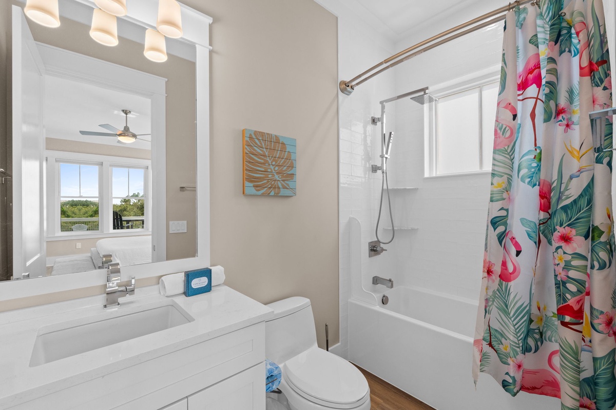 Your bright, modern bathroom features a crisp white design with tropical-inspired touches—fresh towels waiting, a spacious tub-shower combo, and peaceful views through the mirror's reflection.