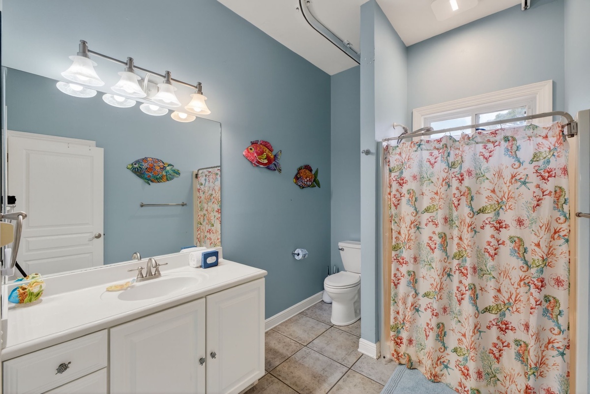 Your coastal-themed bathroom features soothing blue walls, charming sea life art, and a vibrant coral shower curtain that brings ocean vibes to your daily routine.