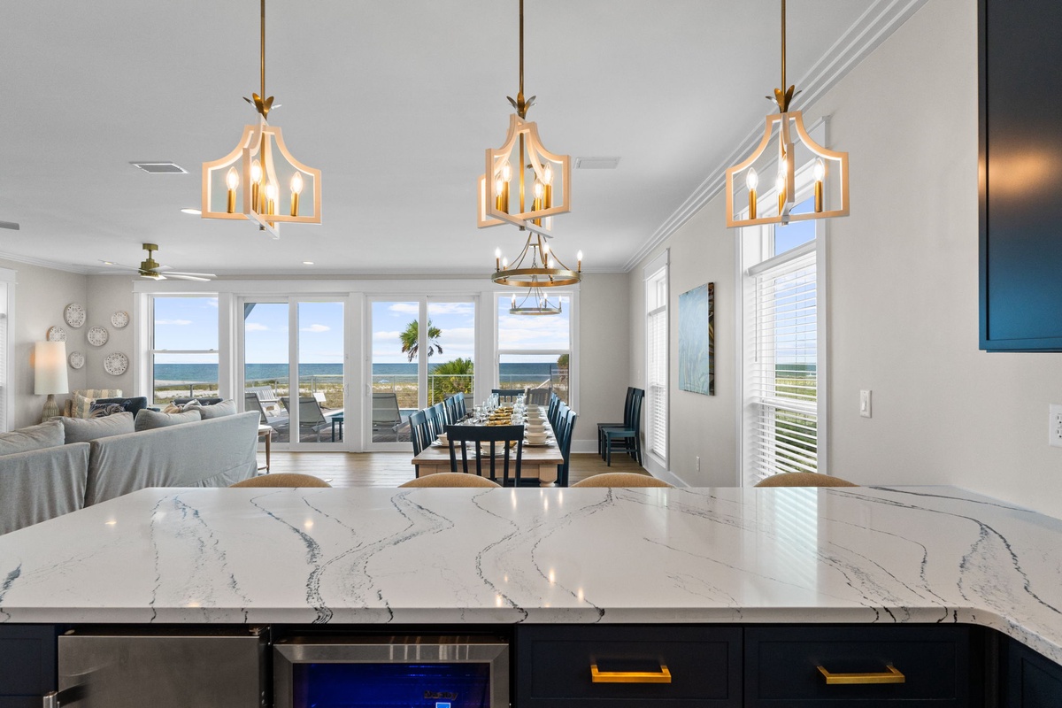 Sunlit open-concept living with stunning ocean views through floor-to-ceiling windows. Elegant chandeliers cast a warm glow over the dining and kitchen areas, creating your perfect coastal escape.