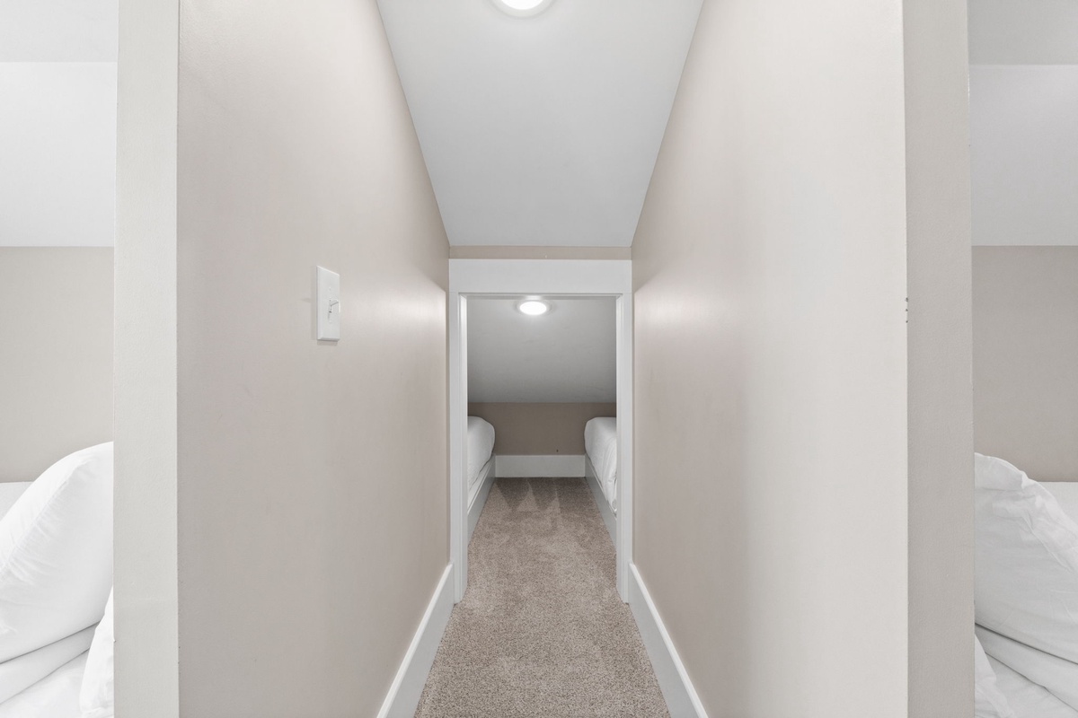 Step into your cozy sleeping nook, where twin beds await in this charming attic-style space with sloped ceilings and soft carpet underfoot.