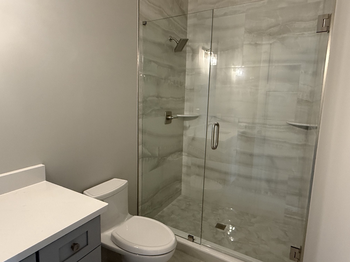 Step into your sleek bathroom featuring a spacious glass-enclosed shower with modern marble-look tiles and thoughtful built-in shelving for your essentials.