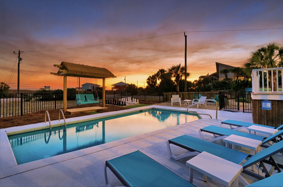 Stunning sunset paints the sky over this tropical pool area with palm trees and comfortable loungers for evening relaxation.