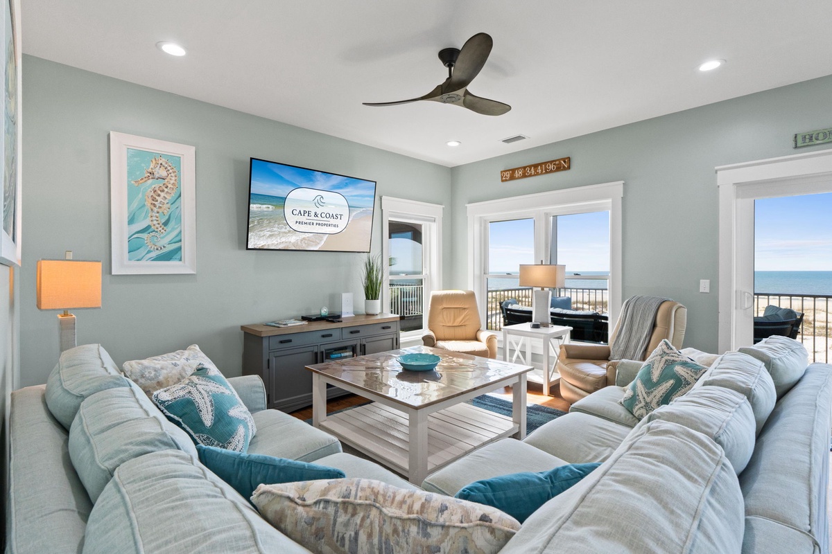 Unwind in your coastal living room where soft sofas face ocean views through glass doors. Relax with the ceiling fan overhead and enjoy beachy décor that brings seaside charm indoors.