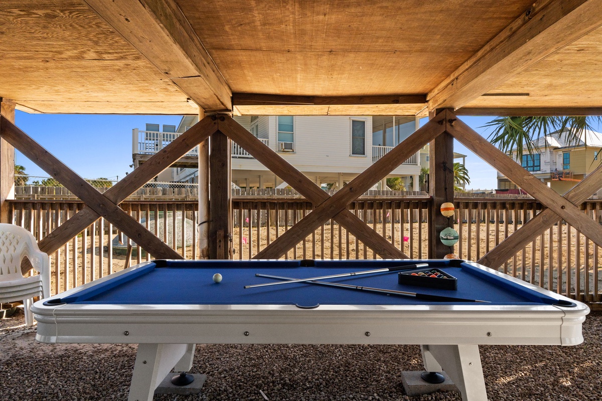 A shaded pool table setup offers relaxed competition with coastal breezes flowing through.