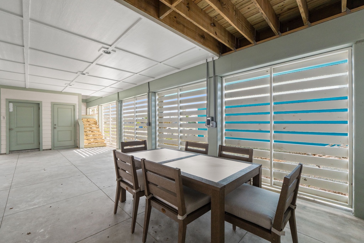 A bright, airy common area features exposed wooden beams and sliding glass doors opening to turquoise poolside views—your perfect spot for casual meals and group gatherings.
