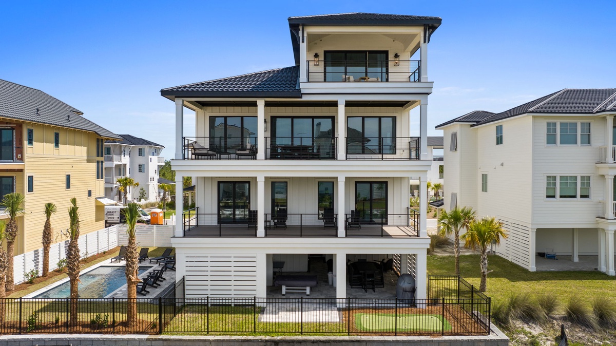 A striking three-story coastal vacation rental featuring multiple private balconies, poolside lounging, and contemporary architecture in a peaceful neighborhood setting.