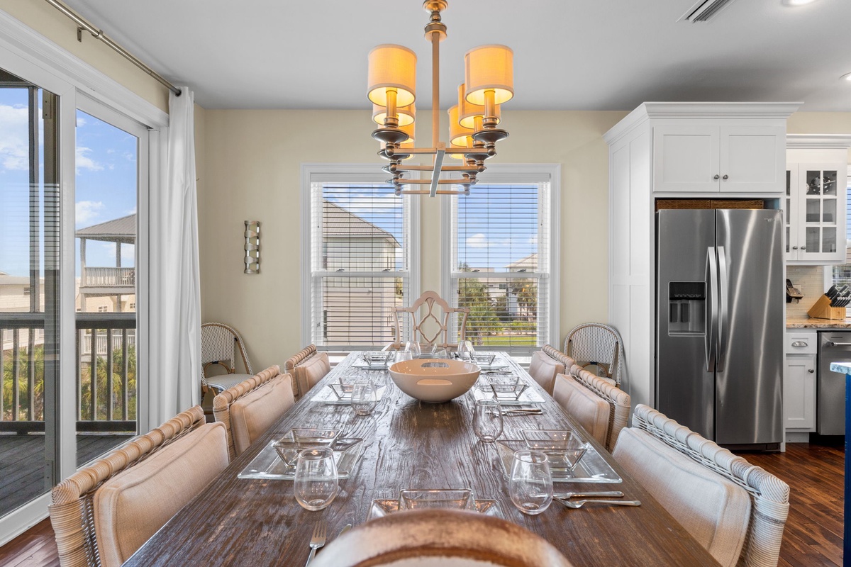 Step into an inviting dining space where you'll gather around a beautifully set table beneath a warm chandelier. Natural light pours through large windows, while the open kitchen awaits your culinary adventures.