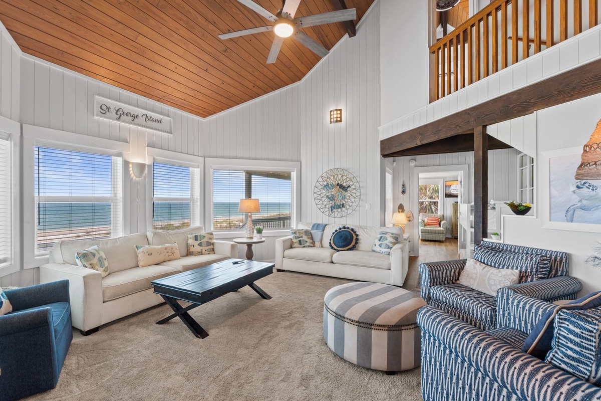 Sink into plush coastal elegance in your vaulted living room, where soaring wood ceilings frame expansive windows overlooking the ocean. Relax on comfortable seating as natural light floods the space, creating your perfect beachside retreat.