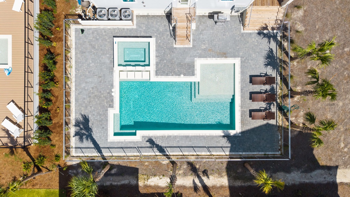 This aerial view showcases the property's inviting swimming pool with adjoining shallow splash area, set within a thoughtfully designed outdoor space featuring tropical landscaping and poolside seating areas.