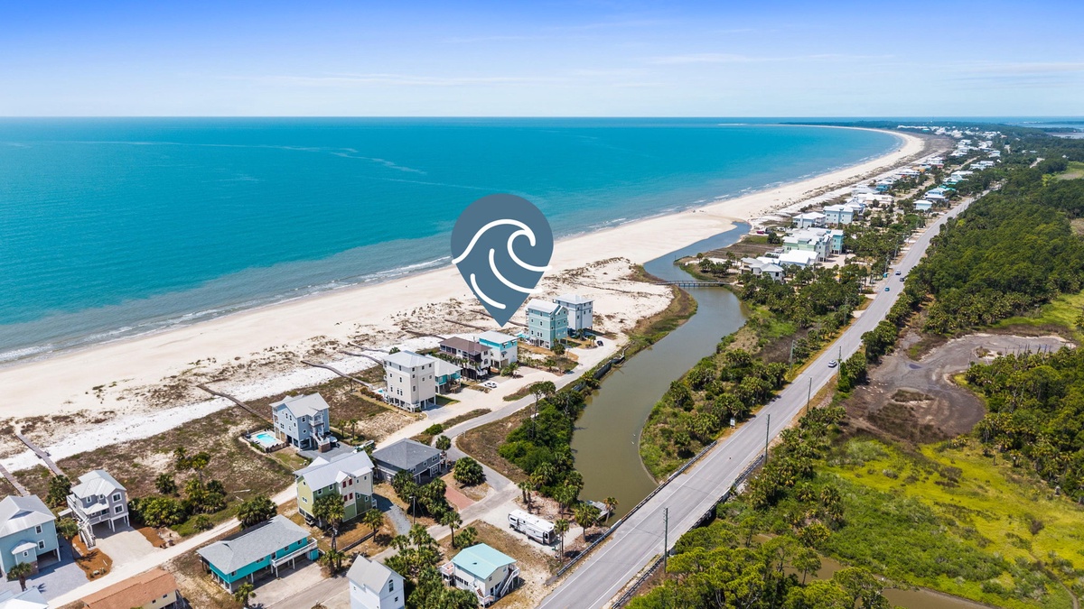An aerial view showcases the pristine beachfront location surrounded by crystal-clear turquoise waters, white sand beaches, and lush coastal landscapes perfect for a peaceful coastal getaway.
