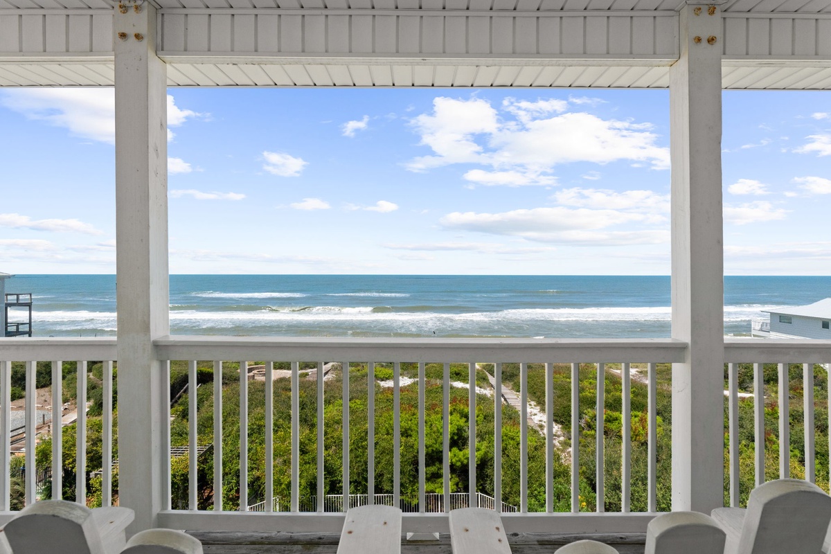Sip your morning coffee from this covered balcony as ocean waves roll gently ashore, framed by coastal greenery and endless blue horizons that stretch beyond the horizon.