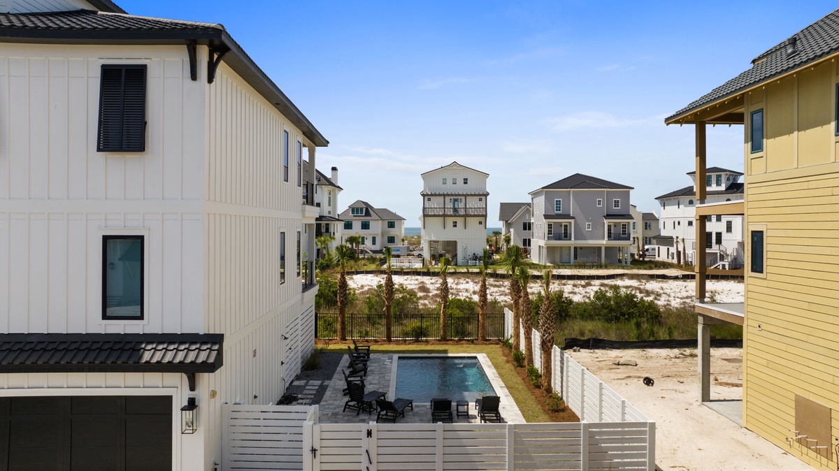 Coastal neighborhood featuring modern beach homes, a private pool with loungers, and natural dune vegetation preserving the serene seaside setting.