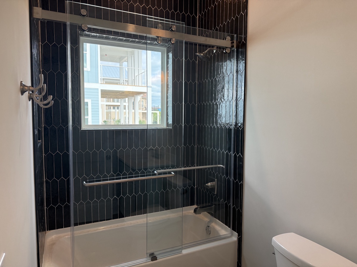 Unwind in your elegant bathroom featuring a glass-enclosed tub-shower combo with stunning dark hexagonal tiles and city views through the window.