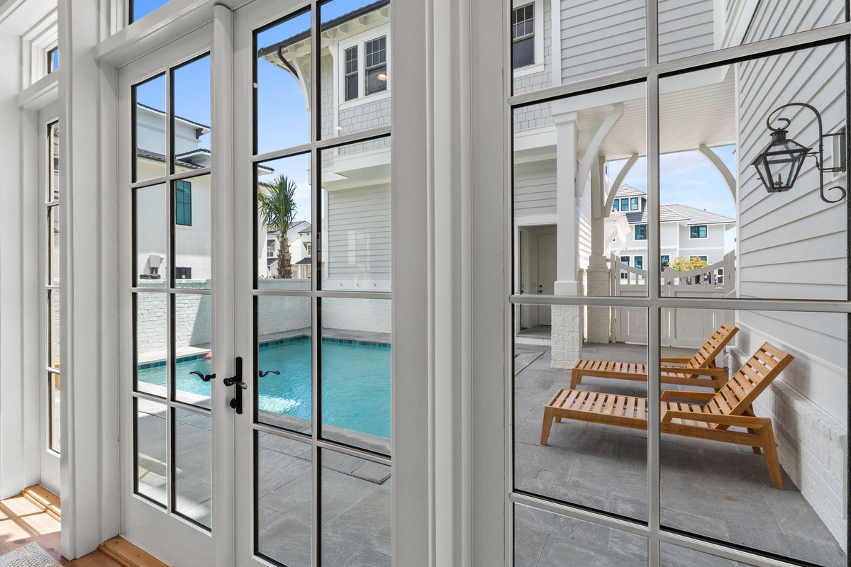 Step through elegant French doors onto your private patio, where poolside loungers await under sun-drenched skies—your personal coastal retreat for lazy afternoons.